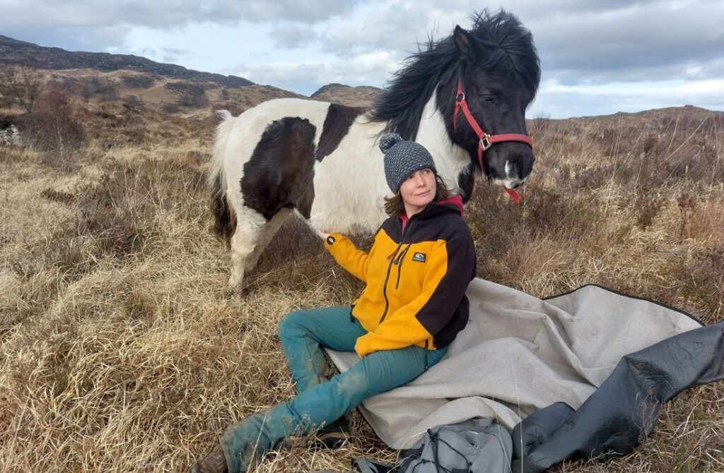 Nicky Ross sitting on a rock in the Scottish Highlilands with her skewbald pony Pixie.